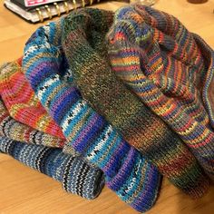 a pile of multicolored knitted hats sitting on top of a wooden table