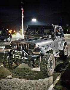 a jeep parked in a parking lot at night with an american flag on the pole