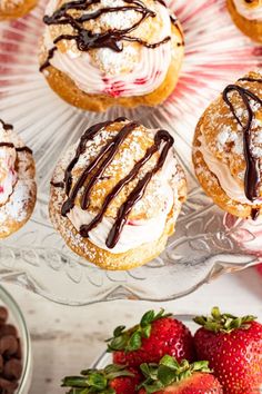 there are many pastries and strawberries on the glass platter with chocolate drizzle