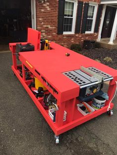 a red work bench sitting in front of a brick building with tools on it's side