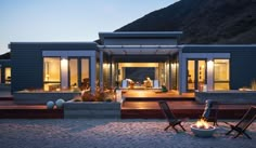 two chairs sitting on top of a sandy beach next to a fire pit in front of a house