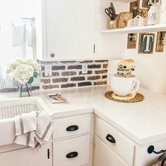 a kitchen with white cabinets and black handles on the counter top, has a brick wall in the background