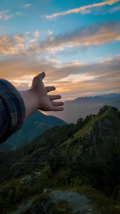 a person's hand reaching out to the sky with mountains and hills in the background