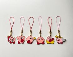 five cartoon keychains with tags attached to them on a white surface and one has a pink lanyard