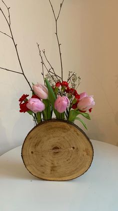 a wooden bowl with flowers in it sitting on a white table top next to a wall