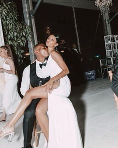 a man and woman sitting on a chair in front of some other people at a party