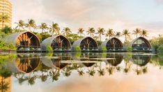 a row of wooden huts sitting on top of a lake next to tall buildings with palm trees in the background