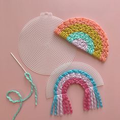 two crocheted rainbows are next to a pair of scissors and yarn on a pink surface