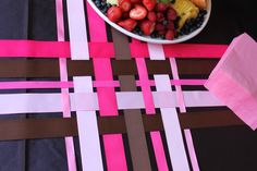 a bowl filled with fruit sitting on top of a pink and brown table cloth next to a plate of strawberries