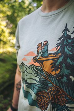 A woman wearing the Dog at Dusk Shirt by Loblola. The shirt shows a woman sitting on a cliff with her dog. There are pine trees, mountains, and pink clouds around. Outdoor Women Outfits, Granola Girl Summer Outfits, Camping Fits, Outdoorsy Outfits, Granola Girl Outfits, Outdoorsy Shirt, Dog Shirt Design, Hiking Shirts Women, Animal T Shirt