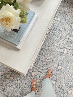 a person standing on a rug next to a book and white flowers in a vase