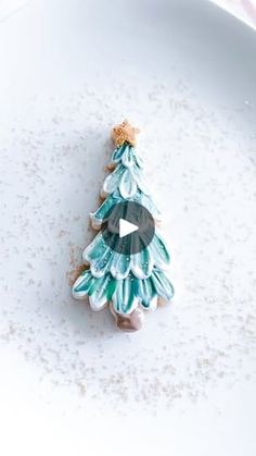 a green and white christmas tree brooch sitting on top of a white plate with snow