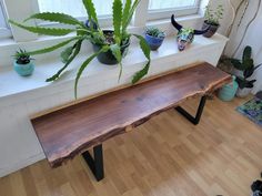 a wooden bench sitting in front of a window next to potted plants on top of a hard wood floor