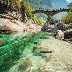 people are standing on a bridge over the water near some rocks and boulders, while others watch