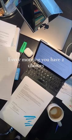 a laptop computer sitting on top of a desk next to papers and a cup of coffee