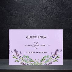 the guest book is sitting on top of a wooden table with purple flowers and greenery