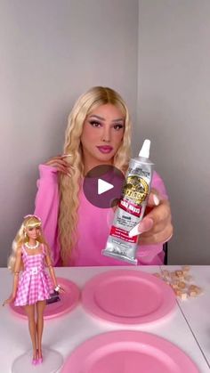 a barbie doll sitting at a table with a bottle of glue on top of it