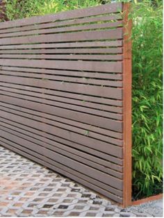 a wooden slatted fence in front of some bushes and plants on the sidewalk