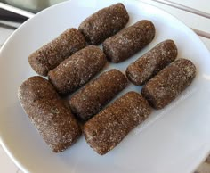 a white plate topped with brown pastries on top of a wooden table next to a window