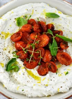 a white bowl filled with whipped cream and tomatoes on top of green leafy garnish