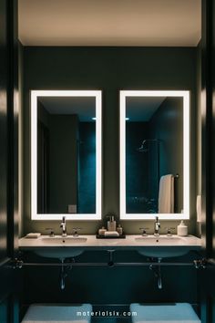 Modern bathroom with double sinks, illuminated mirrors, and dark green walls.