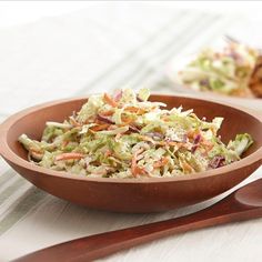 a wooden bowl filled with coleslaw next to a plate of chicken and salad