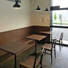 an empty restaurant with wooden tables and chairs in front of large windows that look out onto the street