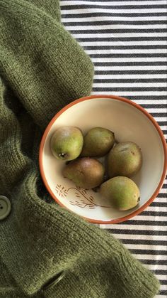 a bowl filled with pears sitting on top of a striped table cloth next to a green sweater