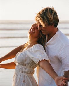 a man and woman standing next to each other on the beach with their arms around each other