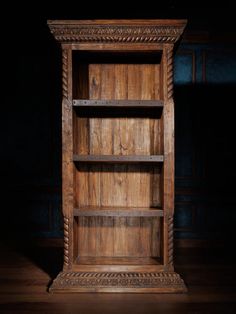 an old wooden bookcase with carvings on the top and bottom shelves, against a dark background