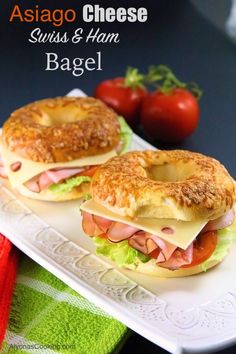 two bagel sandwiches sitting on top of a white plate next to tomatoes and cheese