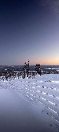 the sun is setting over some snow covered hills and trees in the foreground, with an expanse of deep blue sky above