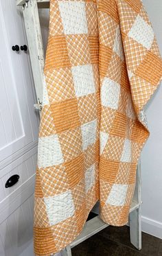 an orange and white checkered blanket sitting on top of a wooden shelf next to a cabinet