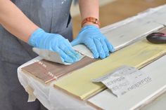 a person in blue gloves and rubber gloves is working on a piece of plywood