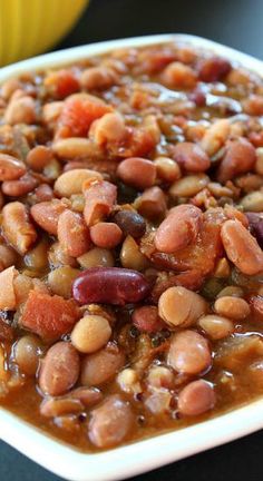 a white bowl filled with beans and meat on top of a black table next to a banana