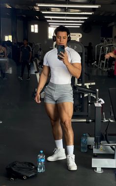 a man in shorts and headphones is looking at his cell phone while standing next to a gym machine