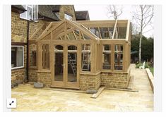 a house being built with wooden framing and windows on the side of the house, in front of a brick building