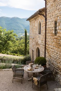 an outdoor table and chairs in front of a stone building with mountains in the background