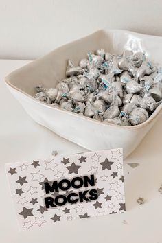 a bowl filled with silver and black stars next to a sign that says moon rocks