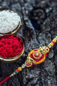 two small metal containers filled with white rice and red colored powder sitting on top of a tree trunk