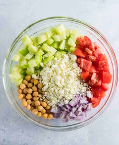 chopped vegetables and chickpeas in a glass bowl on top of a white surface