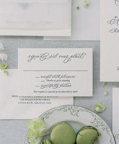 green macaroons are on a plate next to an envelope and some white flowers