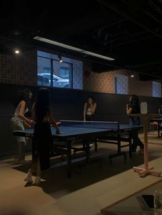 some people are playing ping pong in a dark room with lights on the ceiling