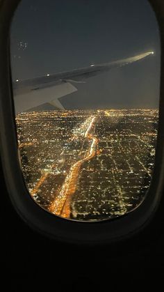 an airplane window with the view of city lights from it's wing at night