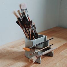 there are many brushes in the holder on the wooden table next to the paintbrushes