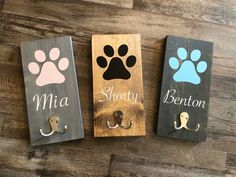 three dog door hangers with paw prints on them, one has a leash and the other has a name