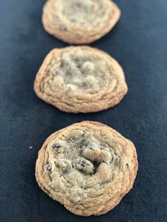 three chocolate chip cookies sitting on top of a black table next to each other with one cookie in the middle