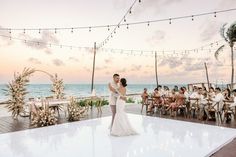 a bride and groom share their first dance on the beach at sunset with guests watching