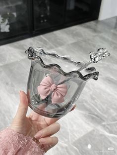 a hand holding a clear glass vase with a pink bow