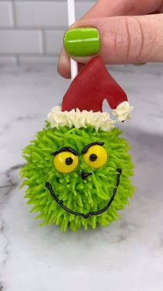 a hand holding a green ball with a santa hat on it's head and eyes